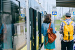 © Iryna - Young couple, hipster man and woman students traveler with backpacks on tram stop going along modern tram.