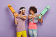 © wayhome.studio  - Funny multiethnic woman and man have fun in gym, fight with rolled up karemats, wear sport clothes, look at each other happily and shout loudly, have regular training together, isolated on purple wall