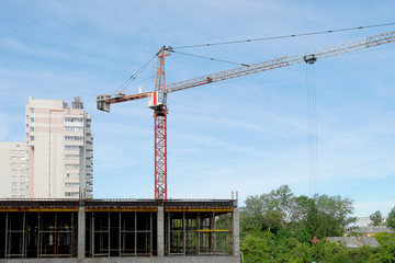 A construction crane lifts a working tool. Boom crane on the construction of a high-rise building. Blue sky, scaffolding/