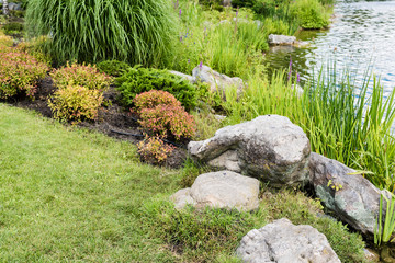 Wall Mural - Stones on green grass near pond and plants in park