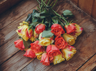 A lush bouquet of flowers. A bouquet of red and yellow roses lies on a wooden table.