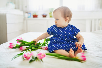 Wall Mural - Baby girl in blue dress playing with bunch of pink tulips