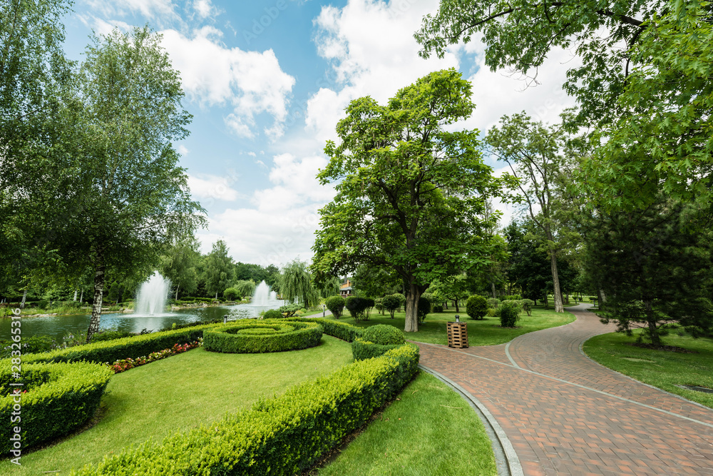 Walkway near green plants, trees and fountains against blue sky Stock ...