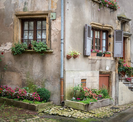 Quaint old stone cottage with plants in windows and bordered by flowers