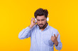 © satura_ - Positive young indian male listens to your favorite online radio using smartphone headphones and high-speed wireless internet on yellow background