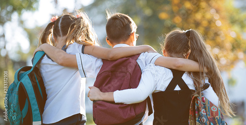 Fotomural school friends a boy and two girls with school backpacks on their backs walk aft