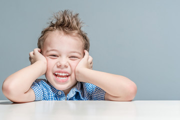 Cute smiling boy sitting at the table on a gray background in the studio. Isolated.