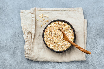 Wall Mural - Rolled oats or oat flakes in wooden bowl on linen textile, top view. Healthy food, dieting, clean eating concept