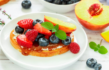 Wall Mural - Delicious breakfast. Delicacy sandwich Toasts with cream cheese or mascarpone, caramel (iris toffee) and fresh berries - blueberries, raspberries, strawberries, peach  and mint. Selective focus