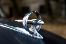 Circular And Futuristic Chrome Bonnet Mascot Or Hood Ornament Of Black 1950's Classic Car Close Up