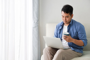 Asian handsome man working with laptop computer and drink coffee in living room happy and smile face