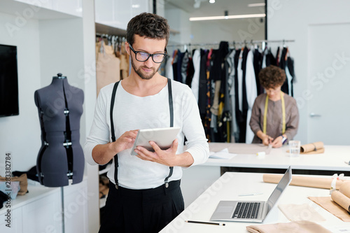 Fotomural Young serious male tailor with tablet looking through online creative ideas