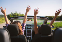 Two Beautiful Young Women Driving In A Convertible With Hands In The Air