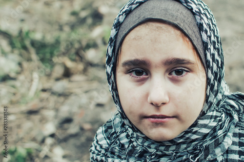 Fotografía a refugee child in the war, a Muslim girl with a dirty face on the ruins, the concept of peace and war, the child is crying and waiting for help
