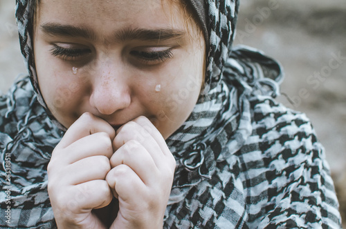 Fotomural a refugee child in the war, a Muslim girl with a dirty face on the ruins, the concept of peace and war, the child is crying and waiting for help