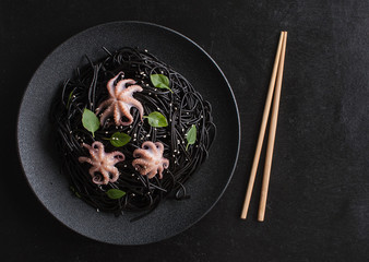 Modern Japanese dinner, Mediterranean cuisine. Black ink spaghetti with black cuttlefish ink, seafood, octopus on a black background. The view from the top. Copy space