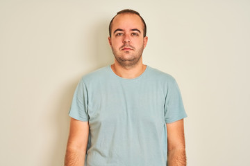 Sticker - Young man wearing blue casual t-shirt standing over isolated white background with serious expression on face. Simple and natural looking at the camera.