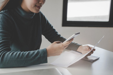 asian young woman using mobile smart phone for scan and payment online with family budget cost bills on desk in home office, plan money cost saving, investment, business finance and expenses concept