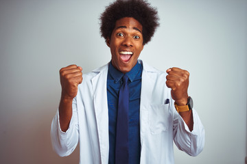 Poster - Young african american doctor man wearing coat standing over isolated white background celebrating surprised and amazed for success with arms raised and open eyes. Winner concept.