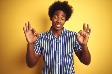 Sticker - American man with afro hair wearing striped shirt standing over isolated yellow background relax and smiling with eyes closed doing meditation gesture with fingers. Yoga concept.