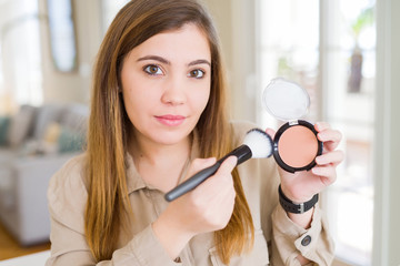 Sticker - Beautiful young woman using make up cosmetics applying powder with a confident expression on smart face thinking serious