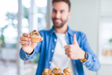 Handsome man eating chocolate chips muffin happy with big smile doing ok sign, thumb up with fingers, excellent sign