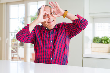 Sticker - Handsome senior man at home doing ok gesture like binoculars sticking tongue out, eyes looking through fingers. Crazy expression.