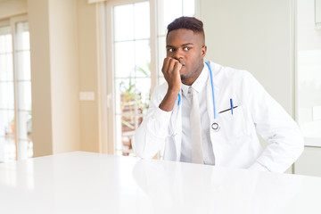 Wall Mural - African american doctor man at the clinic looking stressed and nervous with hands on mouth biting nails. Anxiety problem.