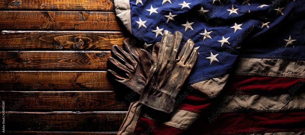 Old and worn work gloves on large American flag - Labor day background - obrazy, fototapety, plakaty 