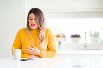 Sticker - Young beautiful woman drinking a cup of coffee at home with hand on stomach because nausea, painful disease feeling unwell. Ache concept.