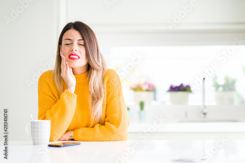 Fotomural Young beautiful woman drinking a cup of coffee at home touching mouth with hand with painful expression because of toothache or dental illness on teeth