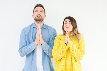 Canvas Print - Young beautiful couple togheter over isolated background begging and praying with hands together with hope expression on face very emotional and worried. Asking for forgiveness. Religion concept.