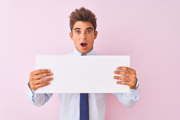 Young handsome businessman holding banner standing over isolated pink background scared in shock with a surprise face, afraid and excited with fear expression