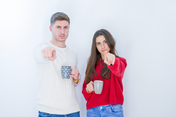 Sticker - Beautiful young couple over white isolated background drinking a cup of coffee pointing with finger to the camera and to you, hand sign, positive and confident gesture from the front