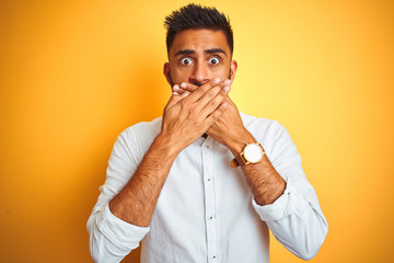 Indian businessman wearing white elegant shirt standing over isolated yellow background shocked covering mouth with hands for mistake. Secret concept.