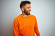 © Krakenimages.com - Young indian man wearing orange sweater over isolated white background looking away to side with smile on face, natural expression. Laughing confident.