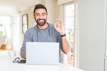 Poster - Handsome hispanic man working using computer laptop doing ok sign with fingers, excellent symbol