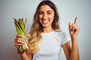 Sticker - Young beautiful woman eating asparagus over grey isolated background very happy pointing with hand and finger to the side