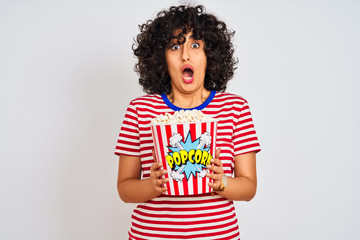 Sticker - Young arab woman with curly hair holding pack of popcorns over isolated white background scared in shock with a surprise face, afraid and excited with fear expression