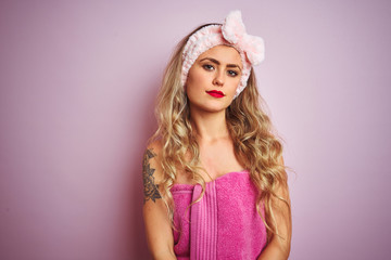 Sticker - Young beautiful woman wearing towel after shower over pink isolated background with serious expression on face. Simple and natural looking at the camera.