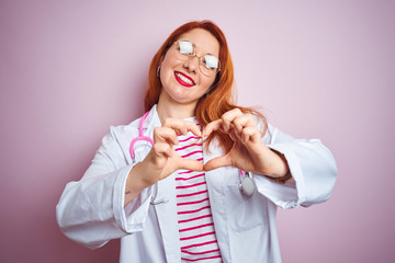 Sticker - Young redhead doctor woman wearing glasses over pink isolated background smiling in love showing heart symbol and shape with hands. Romantic concept.