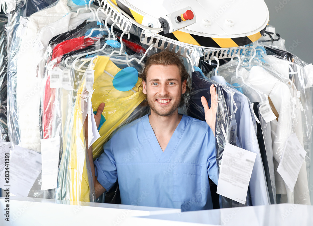 Worker of modern dry-cleaner's near rack with clothes