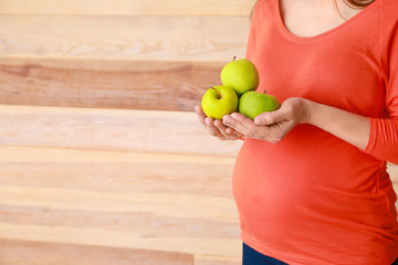 Beautiful pregnant woman with apples on wooden background