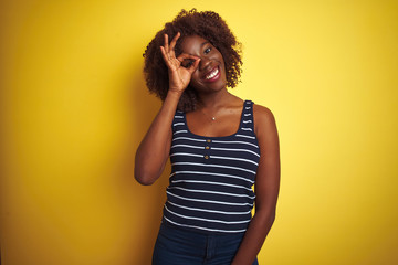 Young african afro woman wearing striped t-shirt over isolated yellow background doing ok gesture with hand smiling, eye looking through fingers with happy face.