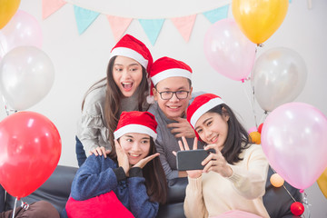 Wall Mural - Young asian people ,a man and three women taking photo by mobile phone in Christmas party.