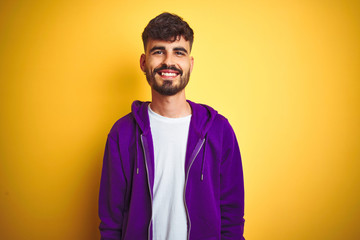 Young man with tattoo wearing sport purple sweatshirt over isolated yellow background with a happy and cool smile on face. Lucky person.