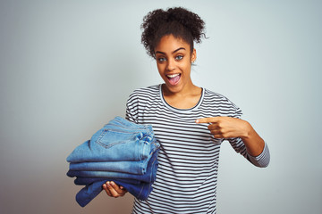 Young african american woman holding stack of jeans over isolated white background very happy pointing with hand and finger