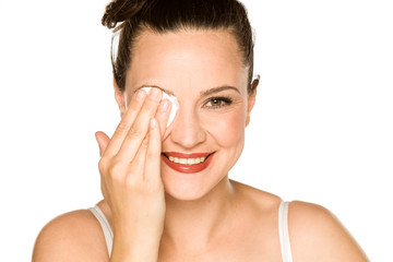 Wall Mural - young happy woman cleans her face with cotton pad on white background