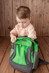 Wall Mural - Little boy with large school bag on wooden background