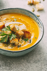 Pumpkin soup in a bowl garnished with pumpkin seed and croutons, close-up.